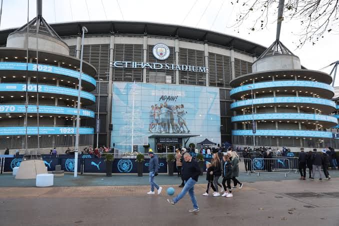 The main entrance of the Etihad Stadium, home of Manchester City, with supporters outside.
