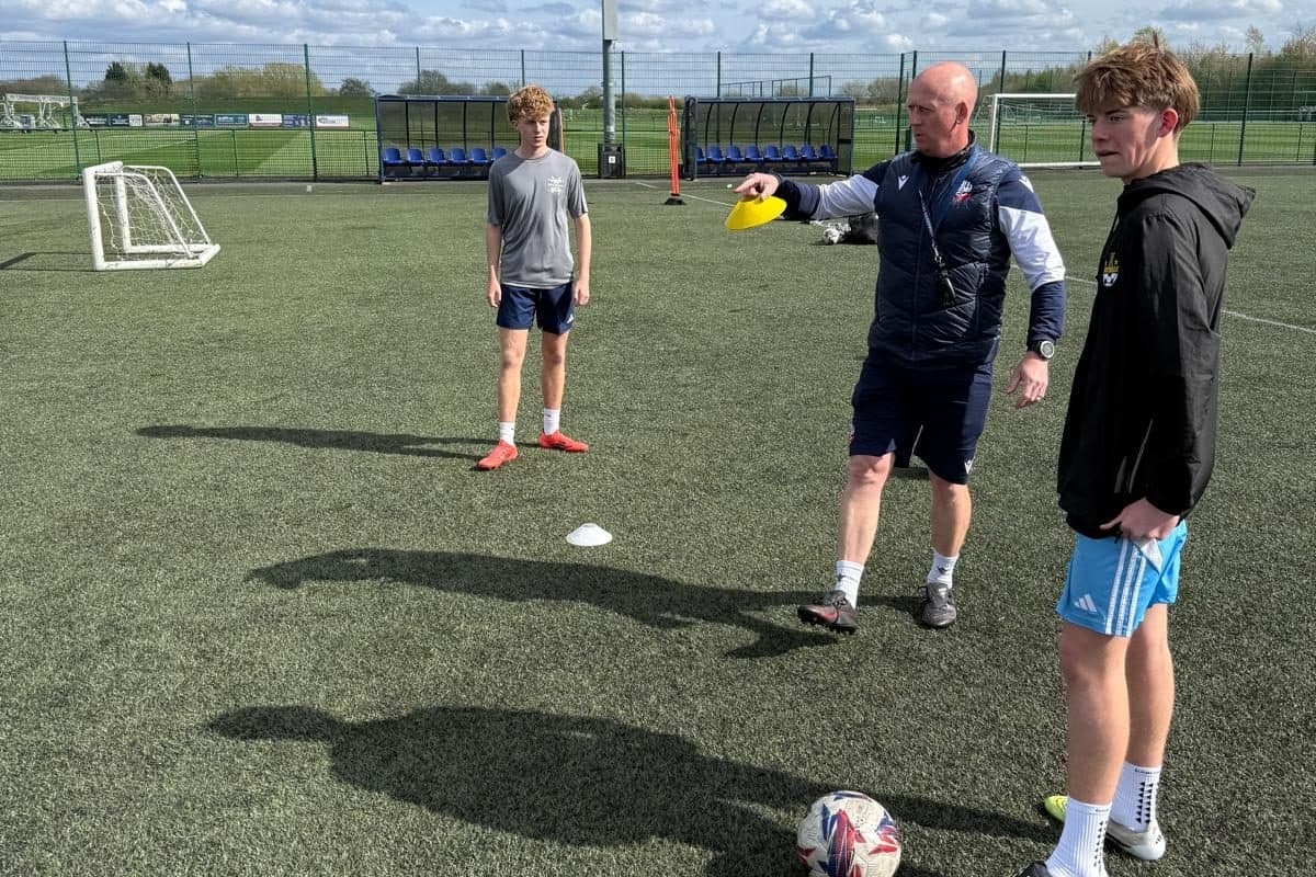 An IPPE academy coach giving feedback to a player on the training pitch during a soccer tour in England